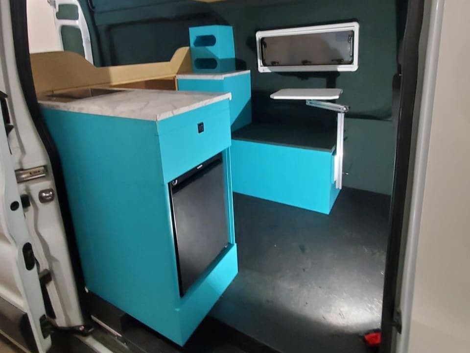 Teal Reliable Campers cabinet kit installed in a camper van, seen through the side door