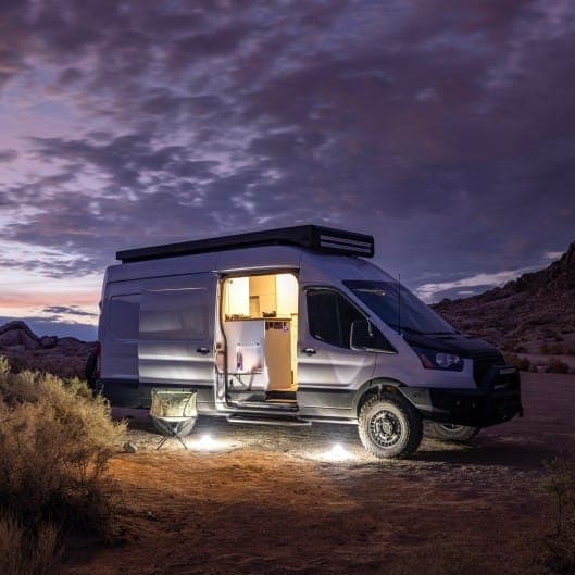 Camper van parked off-grid in the desert at dusk with the awning lit up
